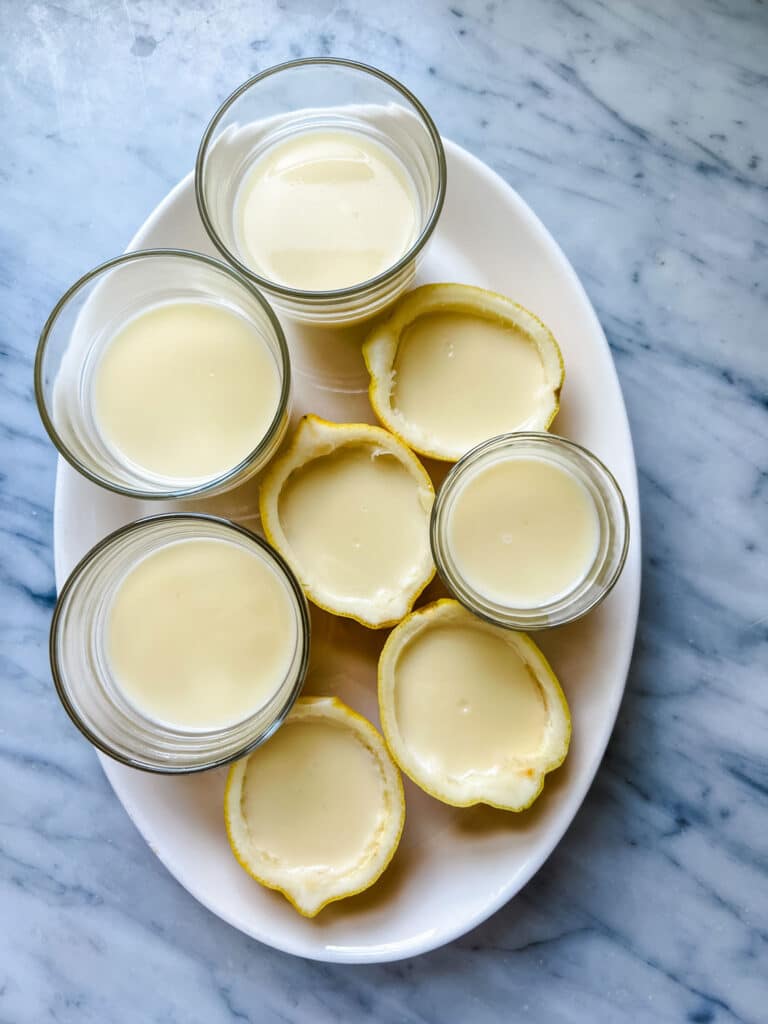 Lemon posset has been poured into small glasses and halves of hollowed-out lemons.