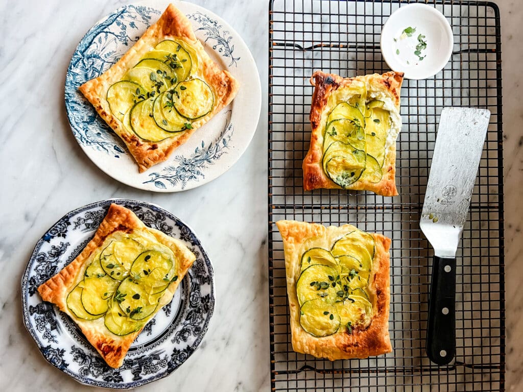Ina Garten's Goat Cheese and Zucchini Tart Recipe on cooling rack with spatula and on two mismatched plates