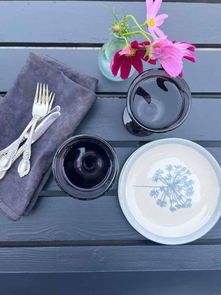  plates, with 2 wine glasses, forks, knives, black napkins. Pink flowers 