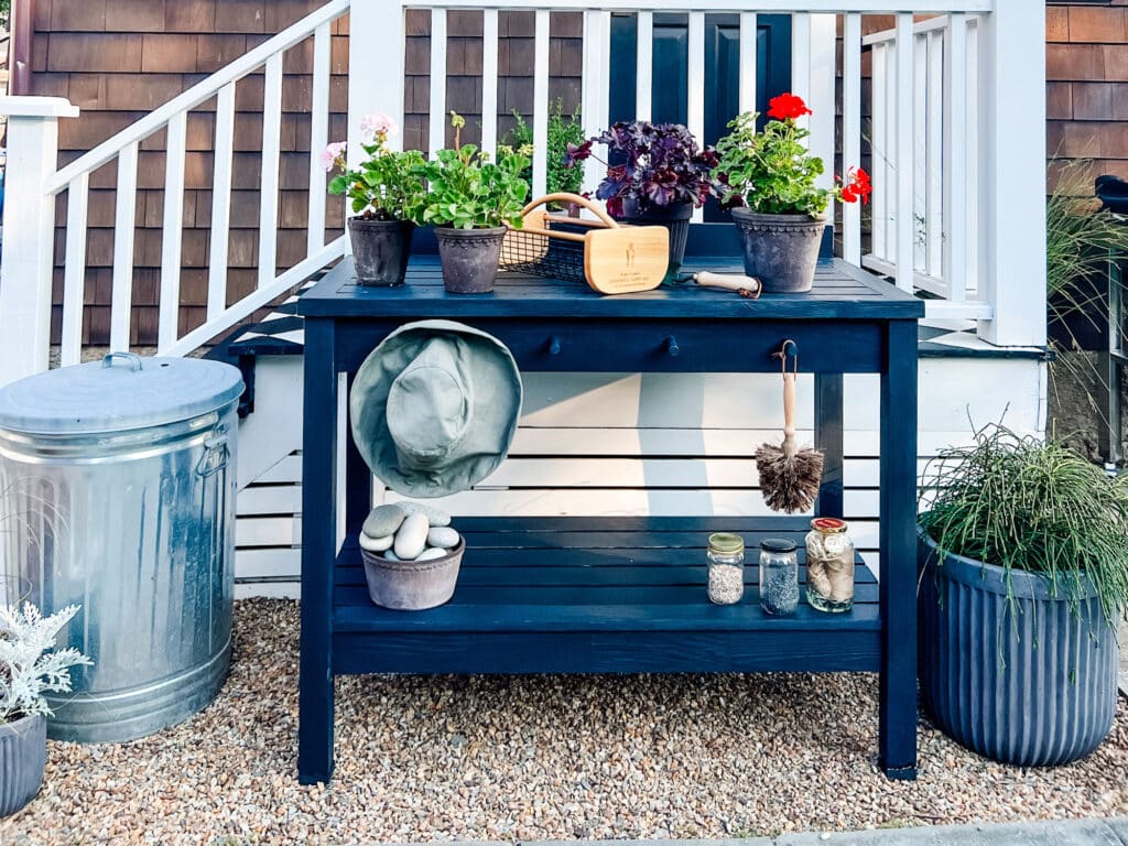 Potting bench painted or stained black on pea gravel with plants and galvanized metal trash can for storage 