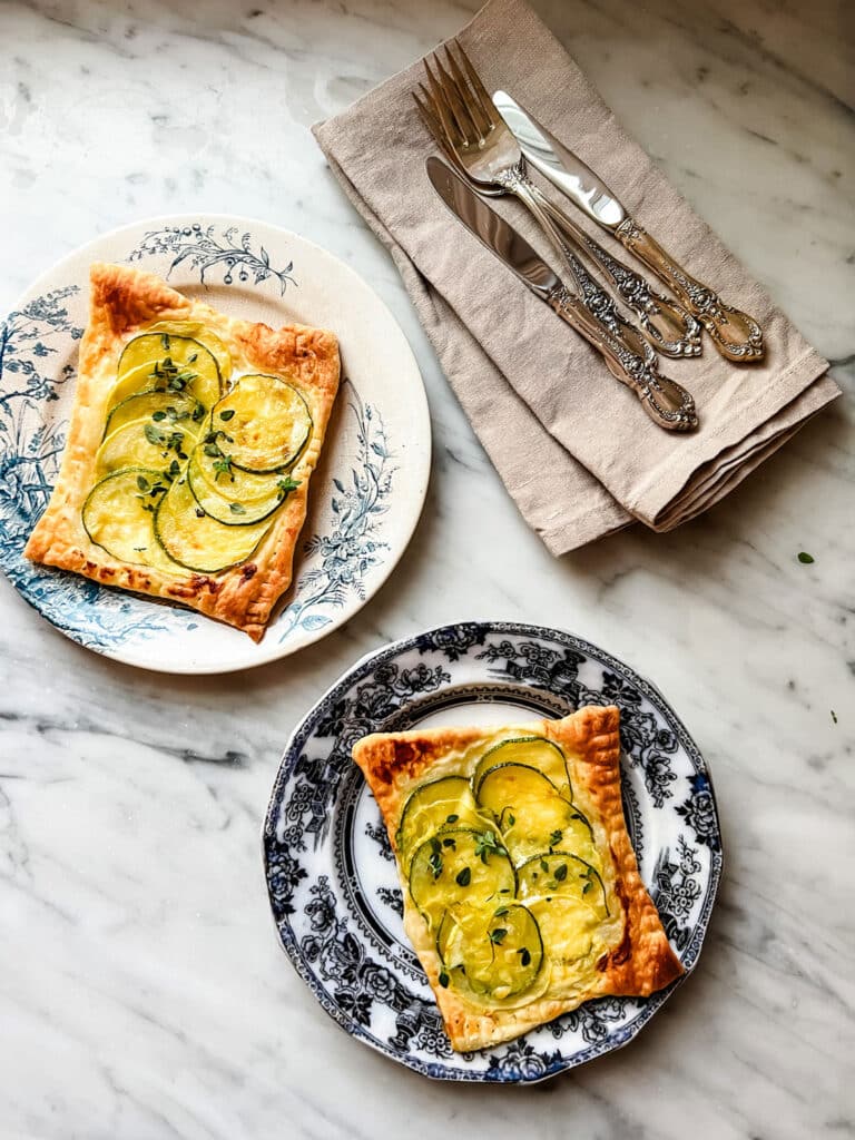 two puff pastry goat cheese zucchini tarts on plates with silverware and linen napkins