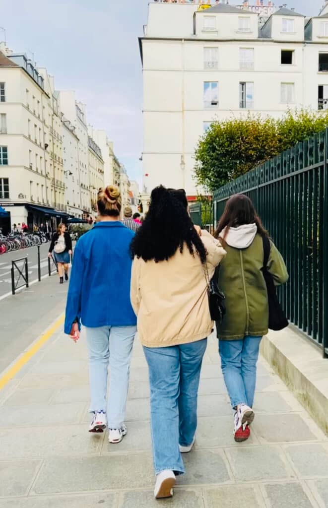 Three women walking side-by-side in Tours, France. One is wearing a vintage blue French chore coat, one a khaki jacket and one with a green jacket with a hoodie underneath it.
