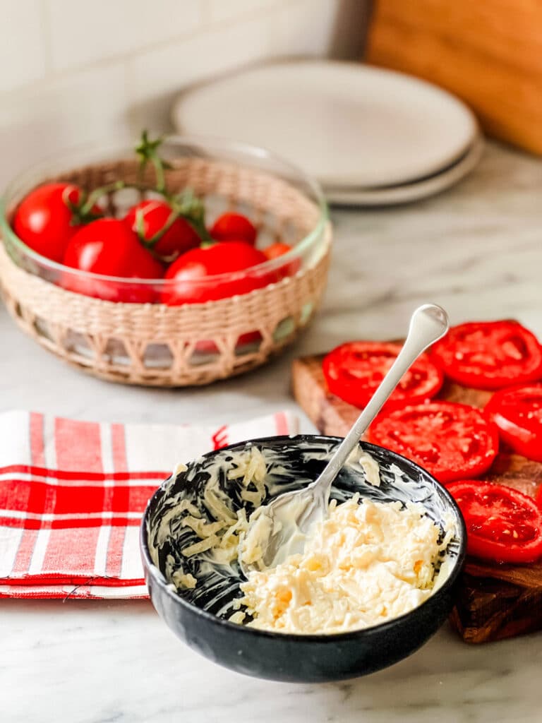 bowl with shredded cheese, mayo, with spoon, basket bowl of tomatoes, red and white plaid tea towel