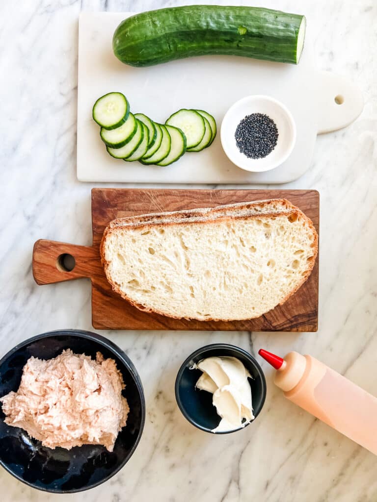 Ingredients for salmon mousse tartines include English cucumbers, black sesame seeds, Italian bread, cream cheese and a sriracha/mayo.