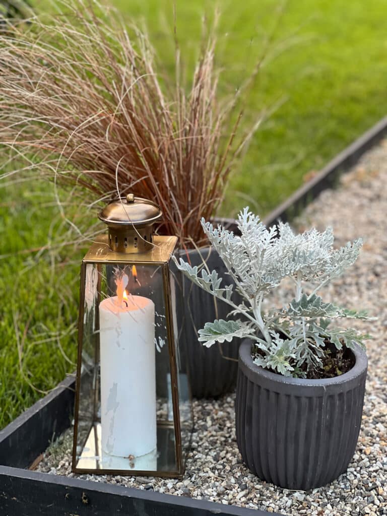 Beach grasses and dusty miller in concrete pots with a brass lantern on a pea gravel patio