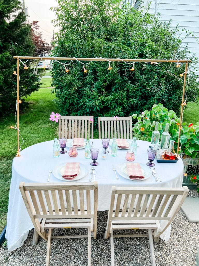 table in garden with lights, candles, pretty linens and glassware with flowers in bottles 