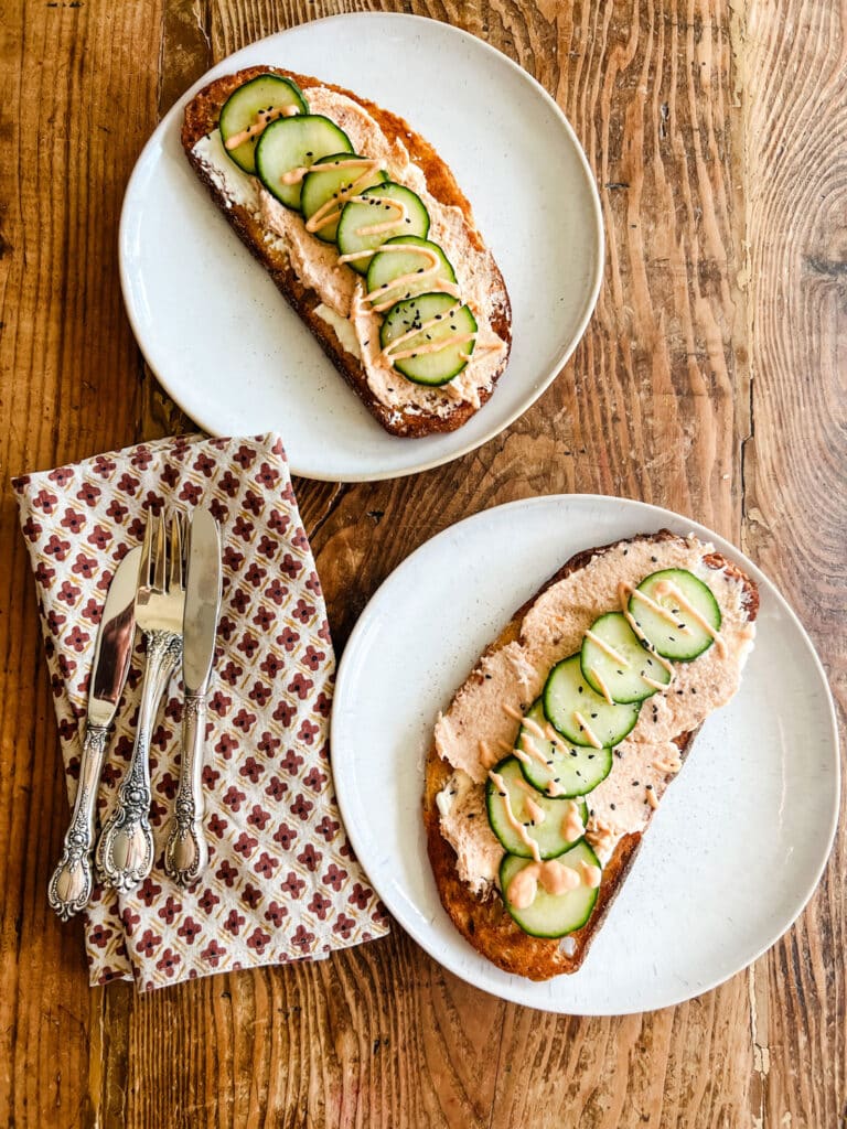 Salmon mousse tartine served on a white plate with silverware and napkins in the background