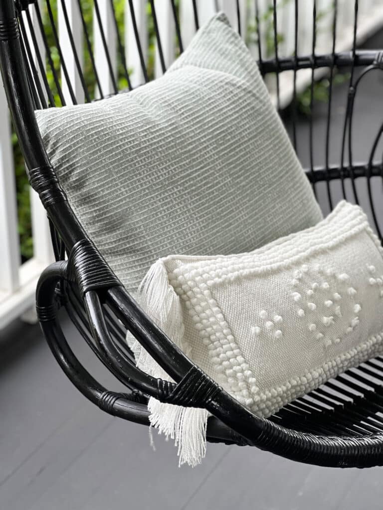 Black hanging rattan swing with white pillow with fringes and mint green textured pillow