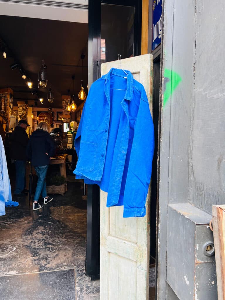A vintage blue French chore coat hanging on an old door in the stall of a Paris flea market