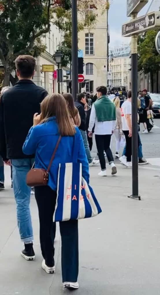 A young woman walking in the streets of Paris wearing a vintage blue French chore coat.