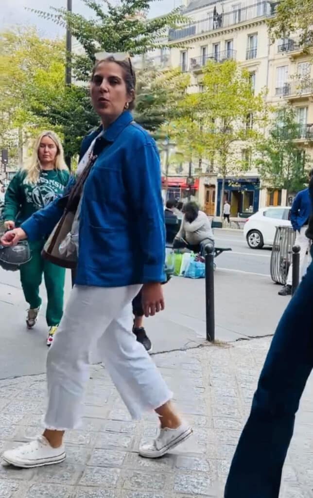 A woman in white jeans and a vintage blue French chore coat strolling through the streets of Paris.