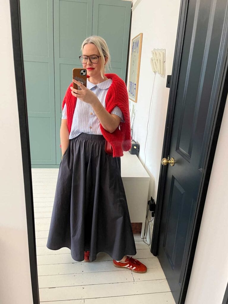 A woman wearing a red cardigan, maxi skirt and red Adidas Gazelles.