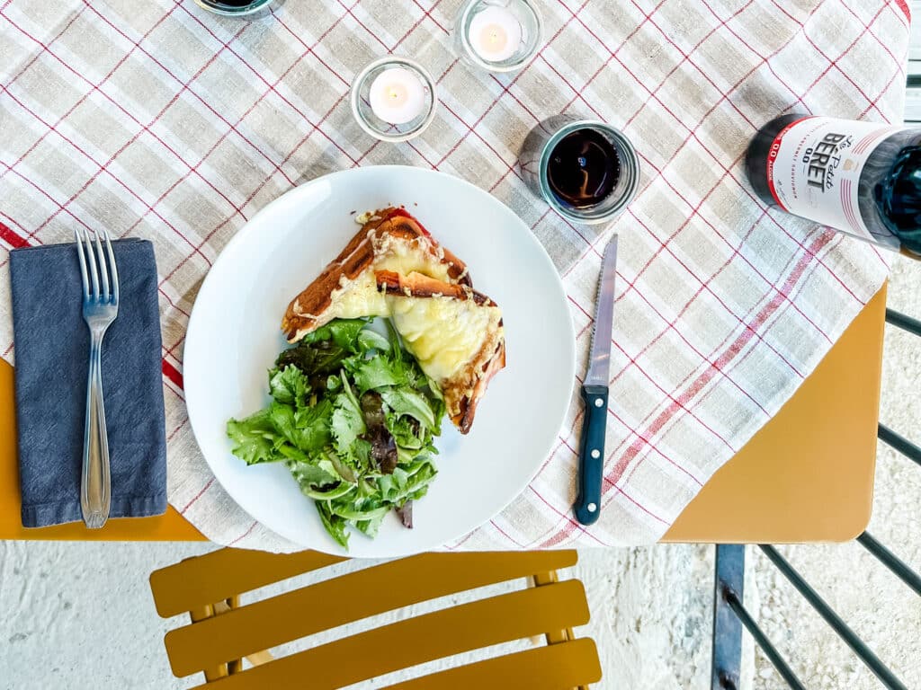 A traditional Croque Monsieur with a small green salad is served on a white plate to bring a little taste of Paris to your kitchen.