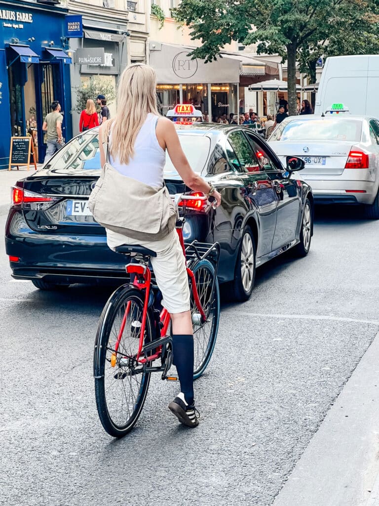 A woman wearing Sambas and black knee socks with a cross-body messenger bag on her bike.