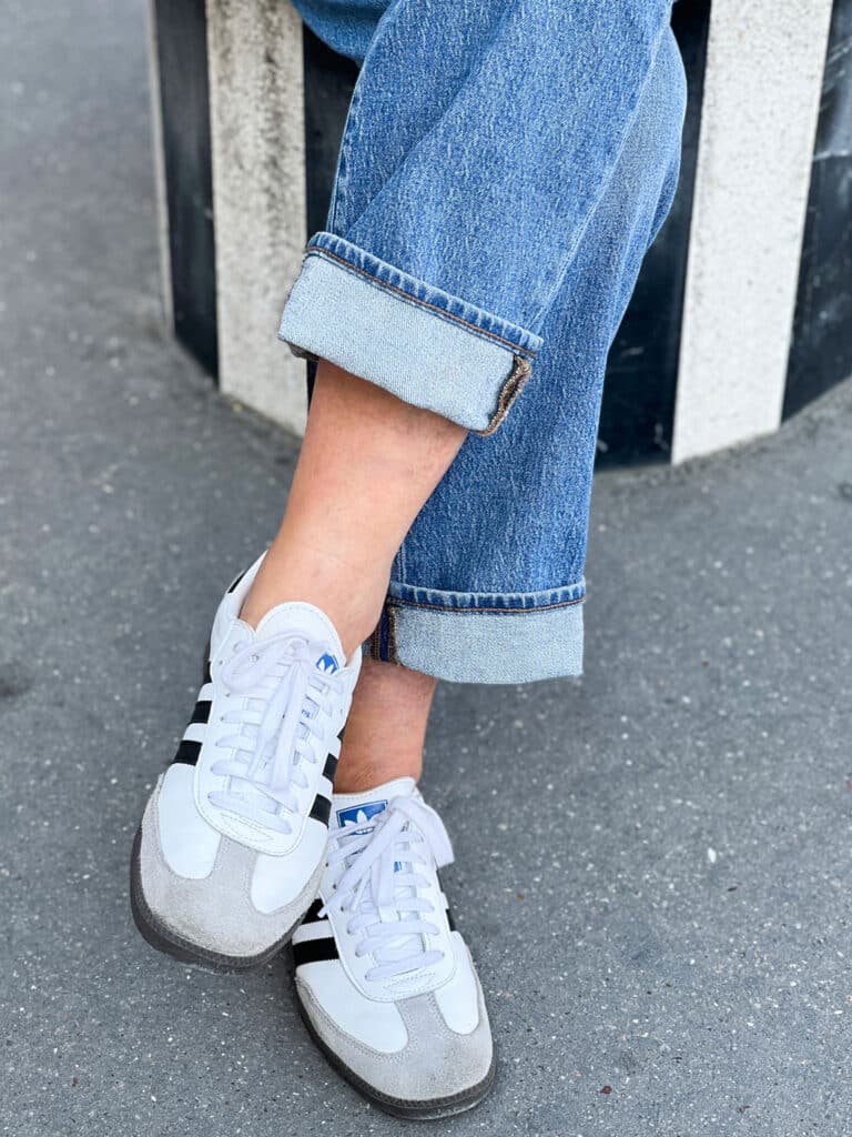 A woman is sitting and wearing cuffed jeans with Adidas Sambas.