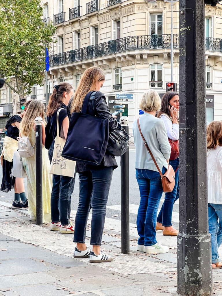 A young woman wearing Adidas Sambas is waiting with a crowd to cross the street.