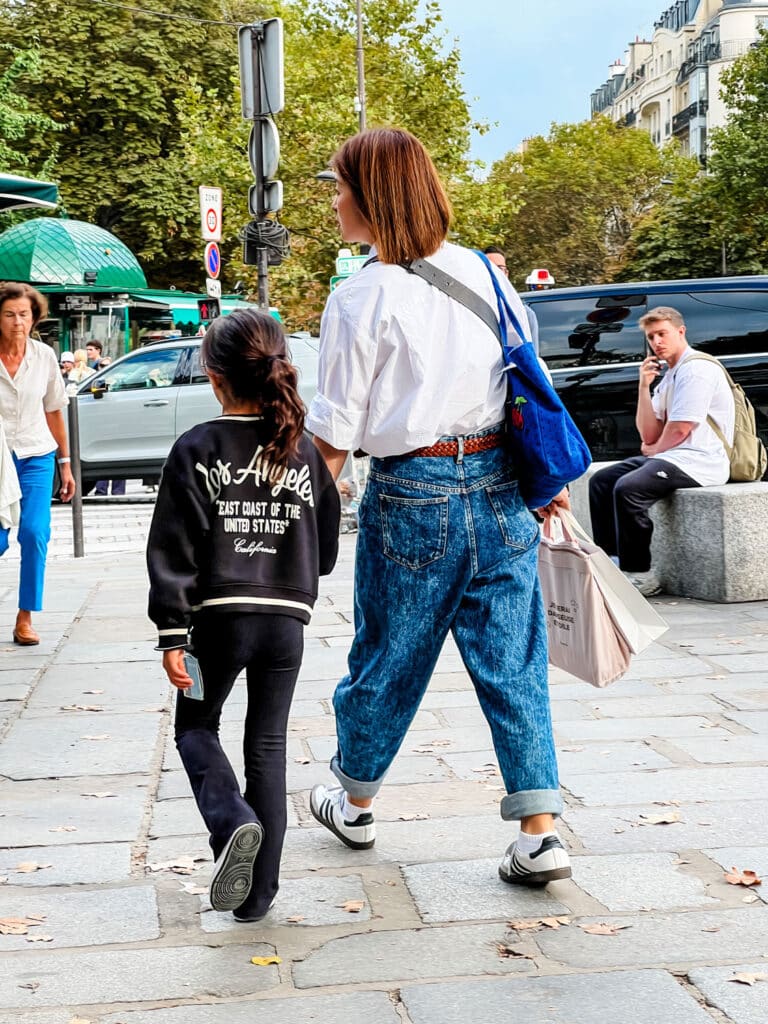 A mother and daughter walking on a street in Paris and the mother is wearing Adidas Sambas.