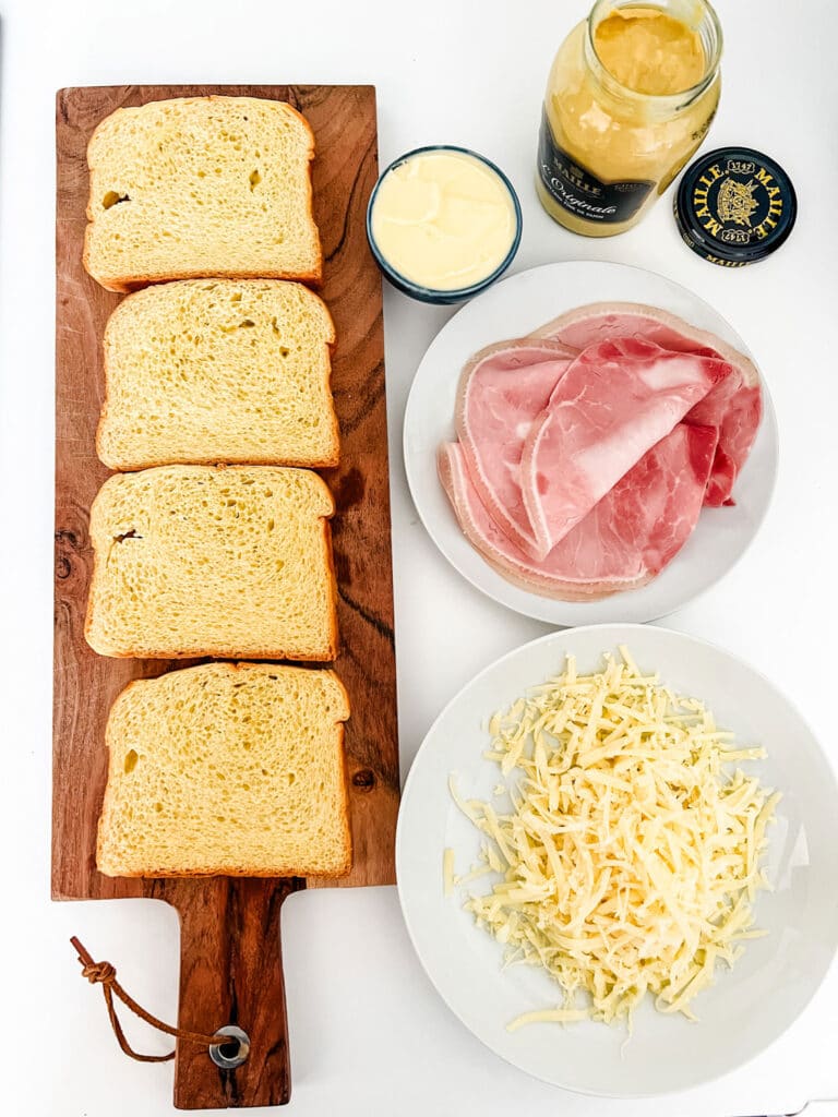 Country bread on a cutting board sits next to all the delicious ingredients for making the Croque Monsieur and bringing a little bit of Paris into your kitchen.