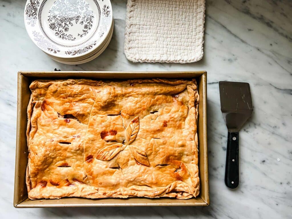 Rustic slab apple pie in a 9" X 12" baking pan next to serving plate and serving spatula.