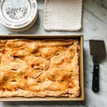 Rustic slab apple pie in a 9" X 12" baking pan next to a serving plate and serving spatula.