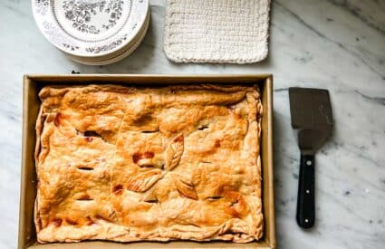 Rustic slab apple pie in a 9" X 12" baking pan next to a serving plate and serving spatula.