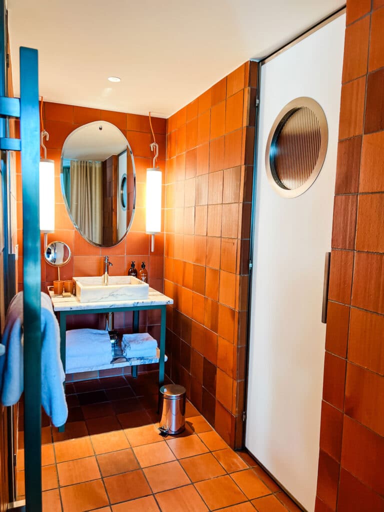 A bathroom at the Mob House Hotel in Paris is decorated with terracotta tiles on the floor and walls. A white sink sit on a marble countertop.