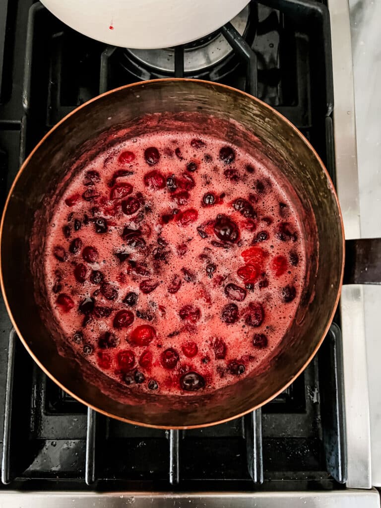 Cranberries, sugar, and orange juice boiling in a copper saucepan.