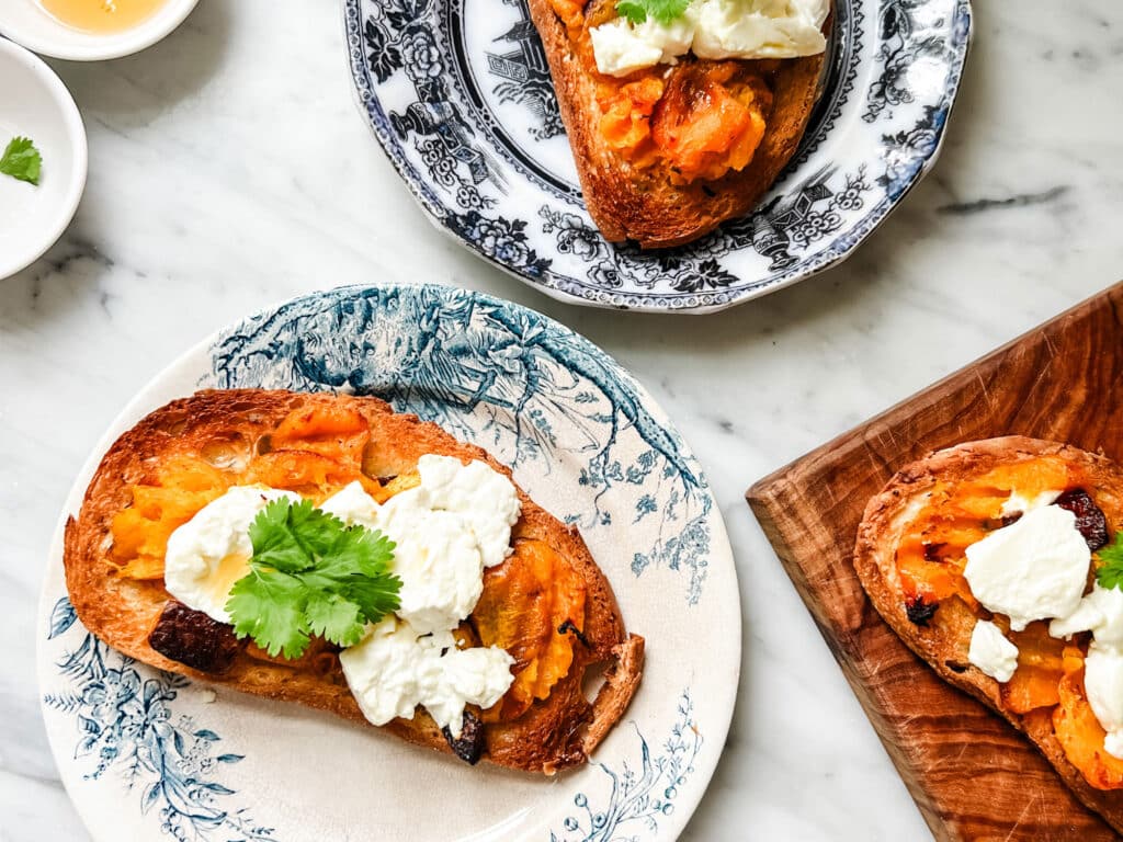 Roasted butternut squash and goat cheese tartines, garnished with cilantro, are served on small blue and white plates.