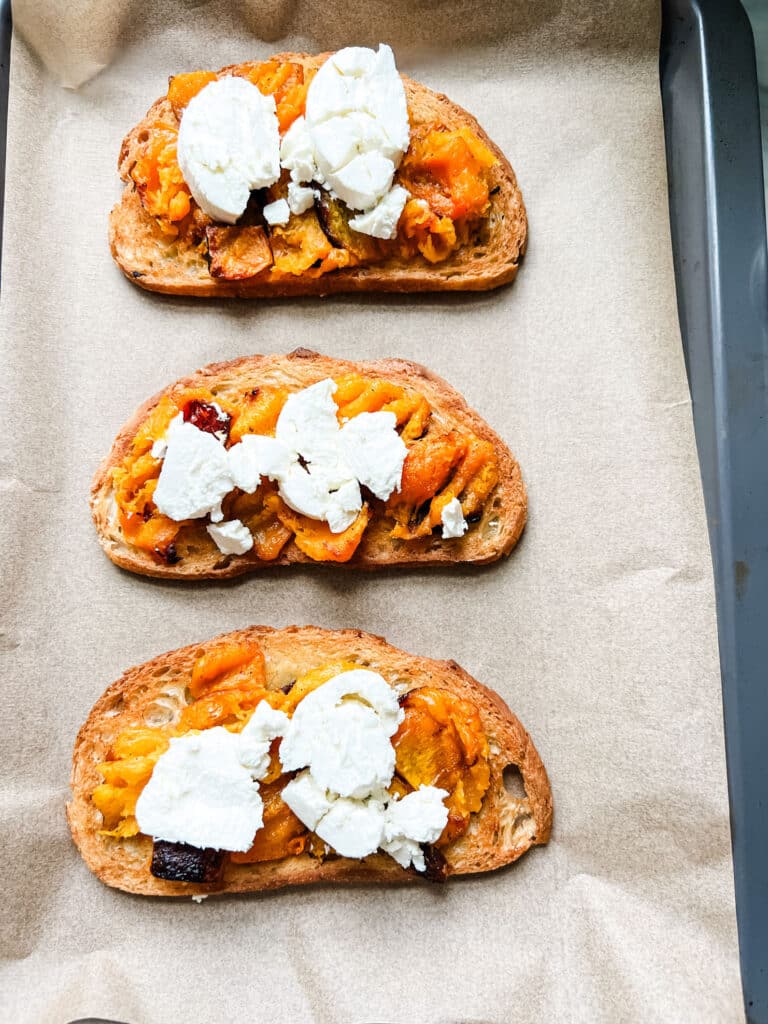Toasted bread topped with roasted butternut squash and goat cheese is on a parchment-lined baking sheet ready to under the broiler for a few minutes.