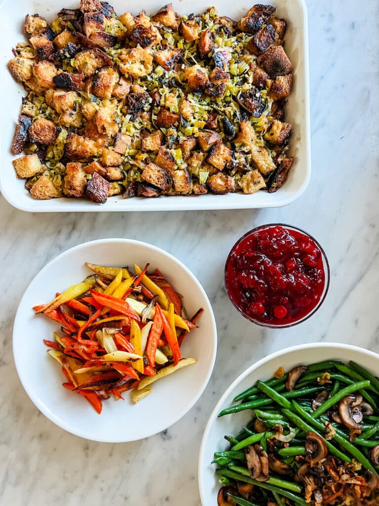 Savory Thanksgiving stuffing, cranberry sauce, maple-glazed carrots, and crispy shallots and mushrooms have been prepared and are ready for serving. 