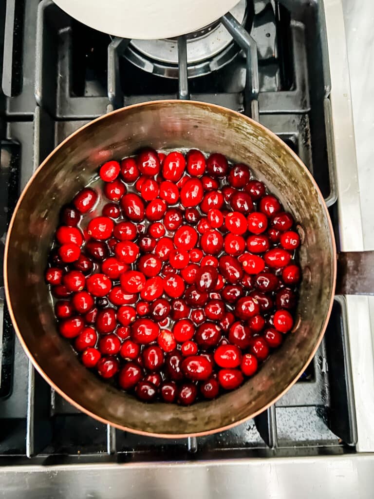 Cranberries, sugar, and orange juice cooking in a copper saucepan.