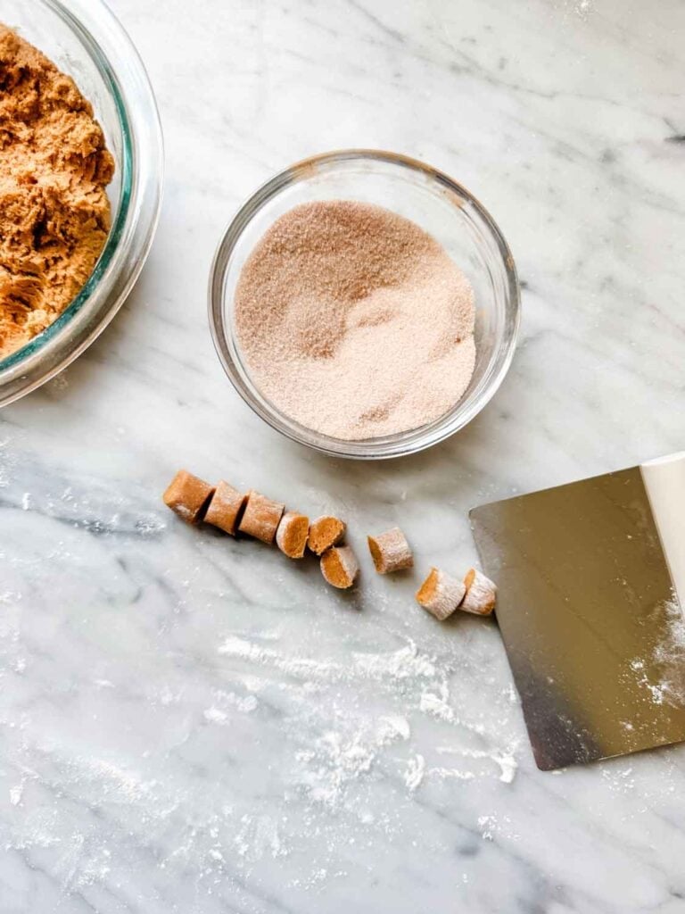 Cookie roll cut into small pieces next to a bowl of cinnmaon sugar.