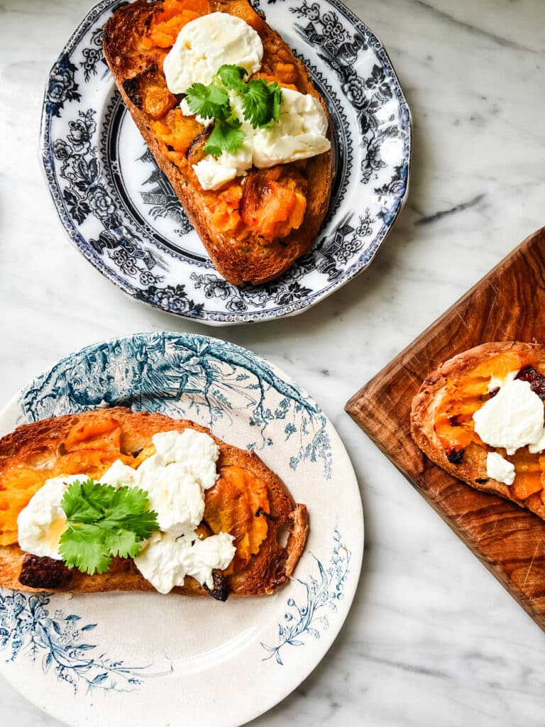 Roasted butternut squash and goat cheese tartines are served on small blue and white plates.