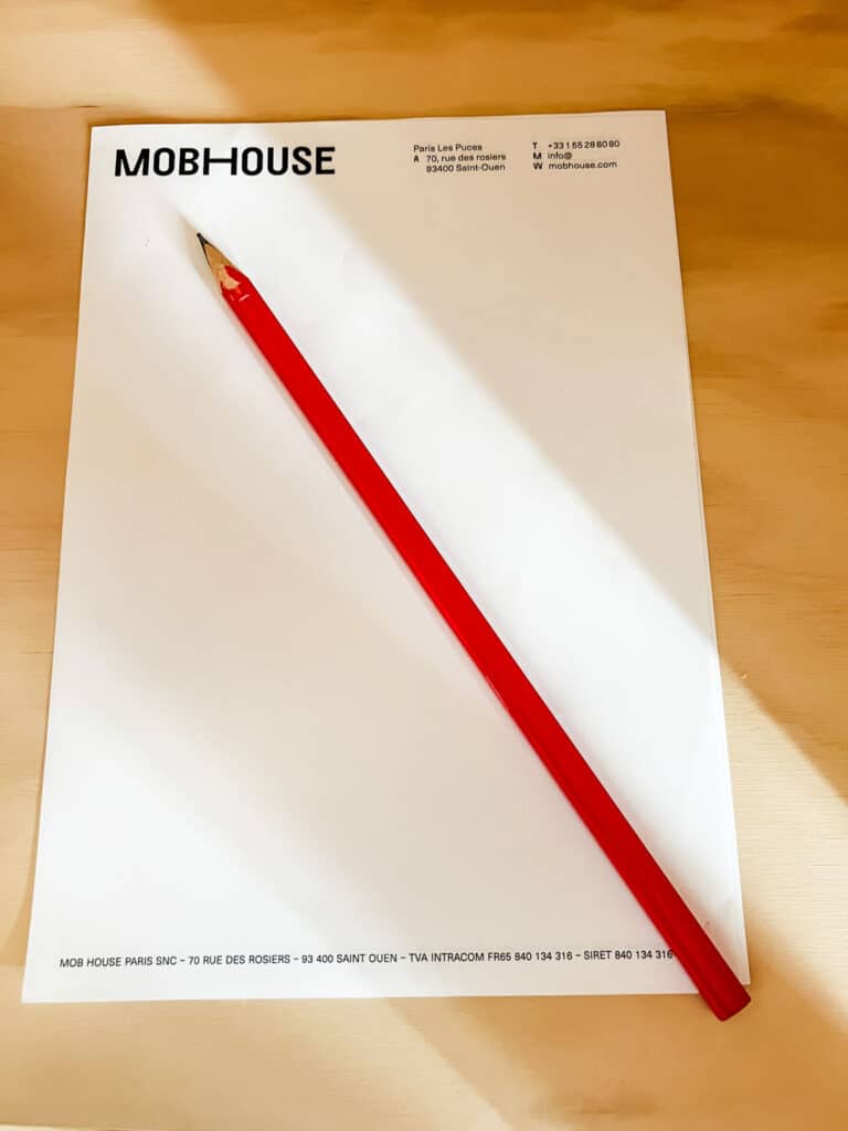 A Mob House Hotel notepad and a super long red pencil sit on a wooden table at the Mob House Hotel Paris.
