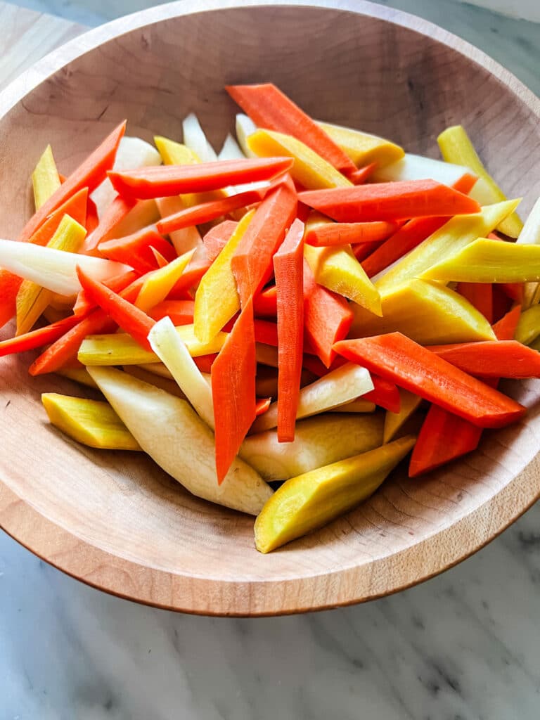Peeled and cut yellow and orange carrots are in a wood mixing bowl.