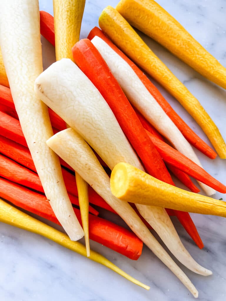 Yellow and orange carrots have been peeled and are sitting on a marbled countertop.