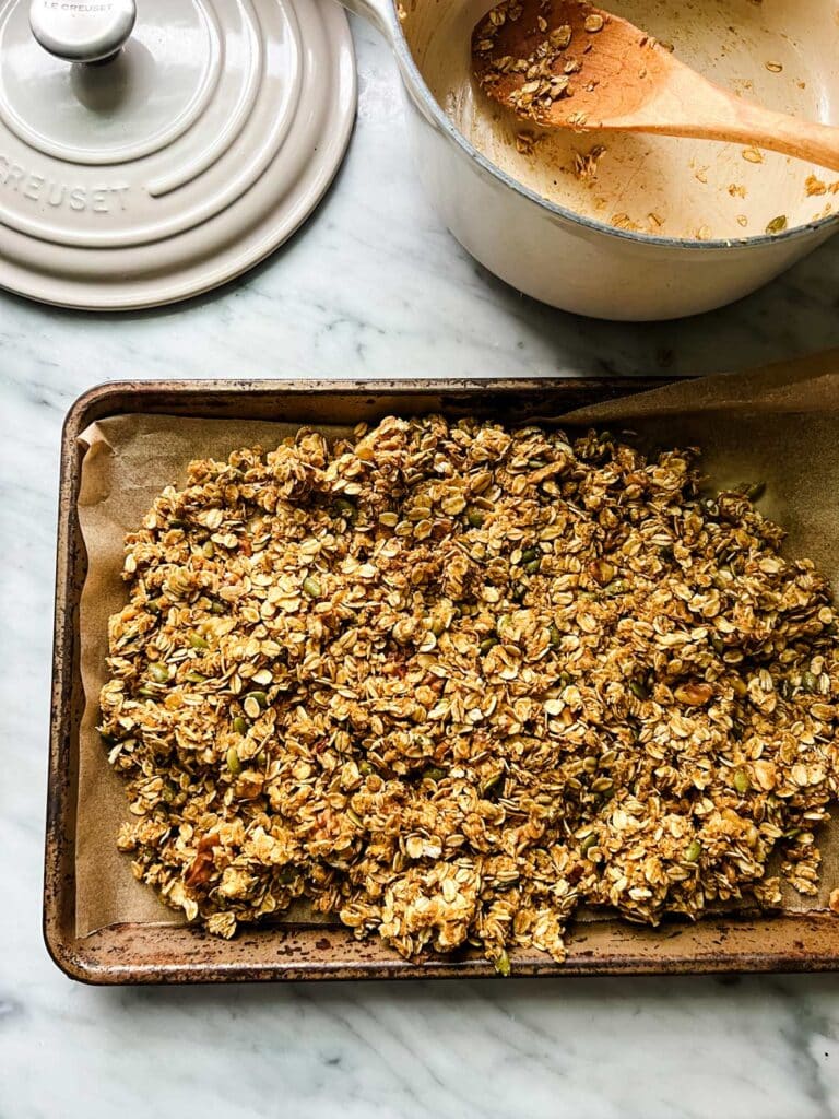 pumpkin granola on sheet pan, with Le Creuset pot on counter with lid
