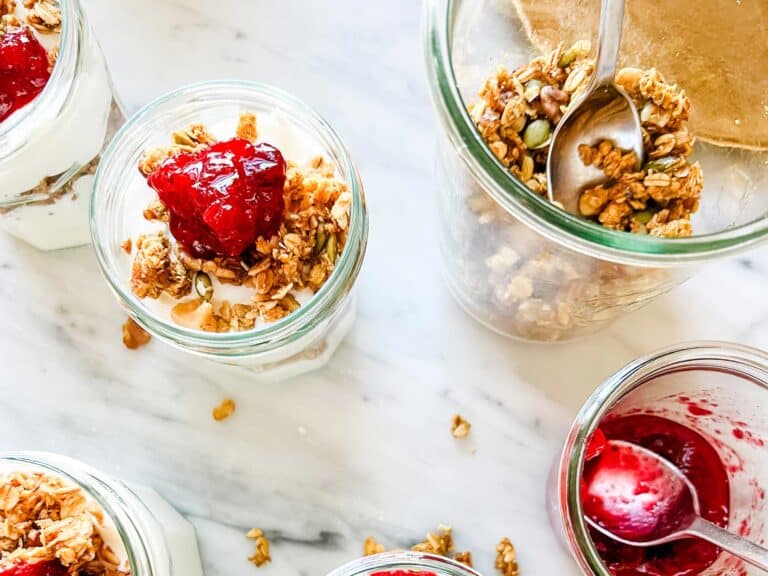 Jars with pumpkin granola and yogurt, topped with cranberry sauce.