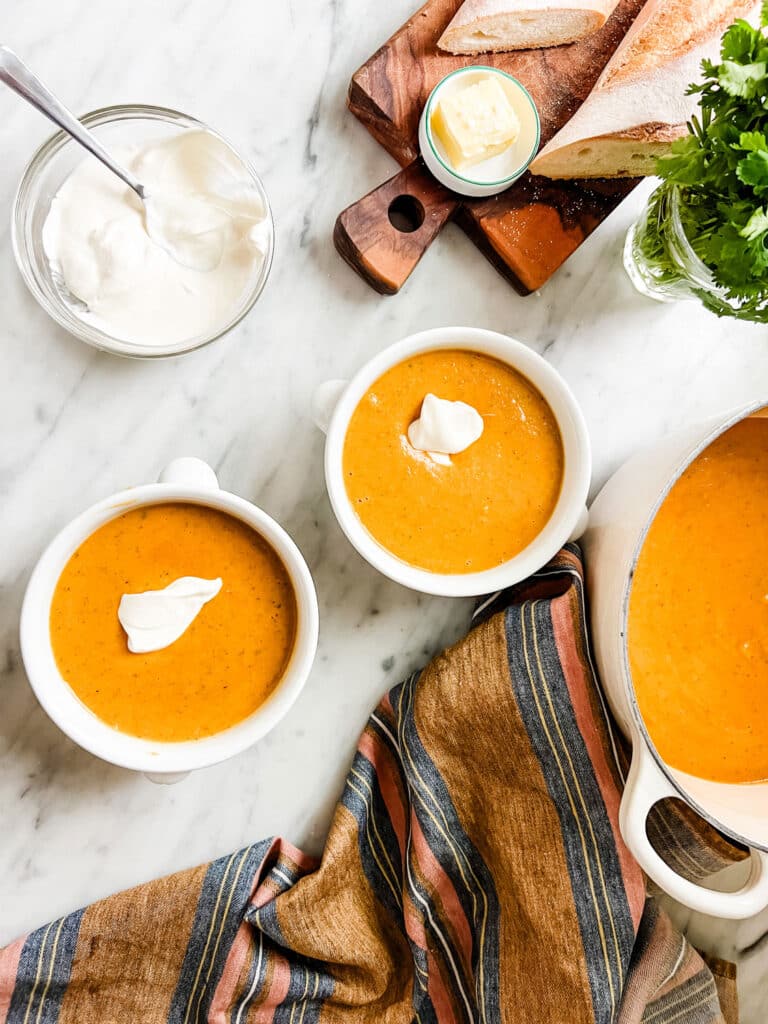 Bowls of pumpkin soup and fresh baguette with butter are ready to be served.
