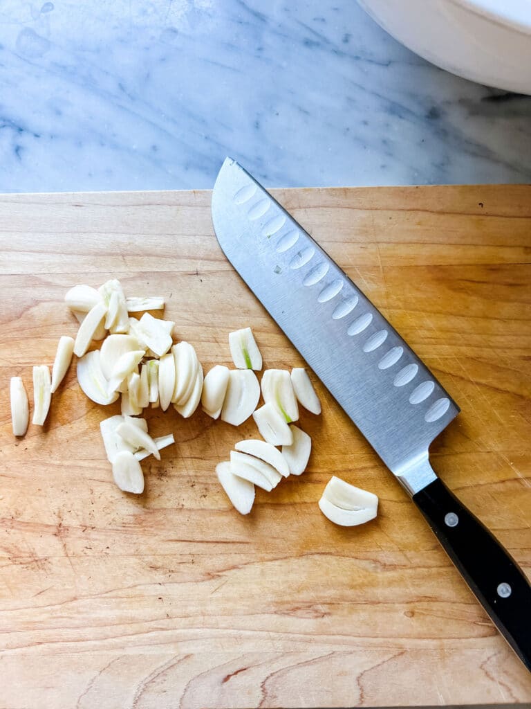 Freshly sliced garlic sits next to a kitchen knife on a wooden cutting board.