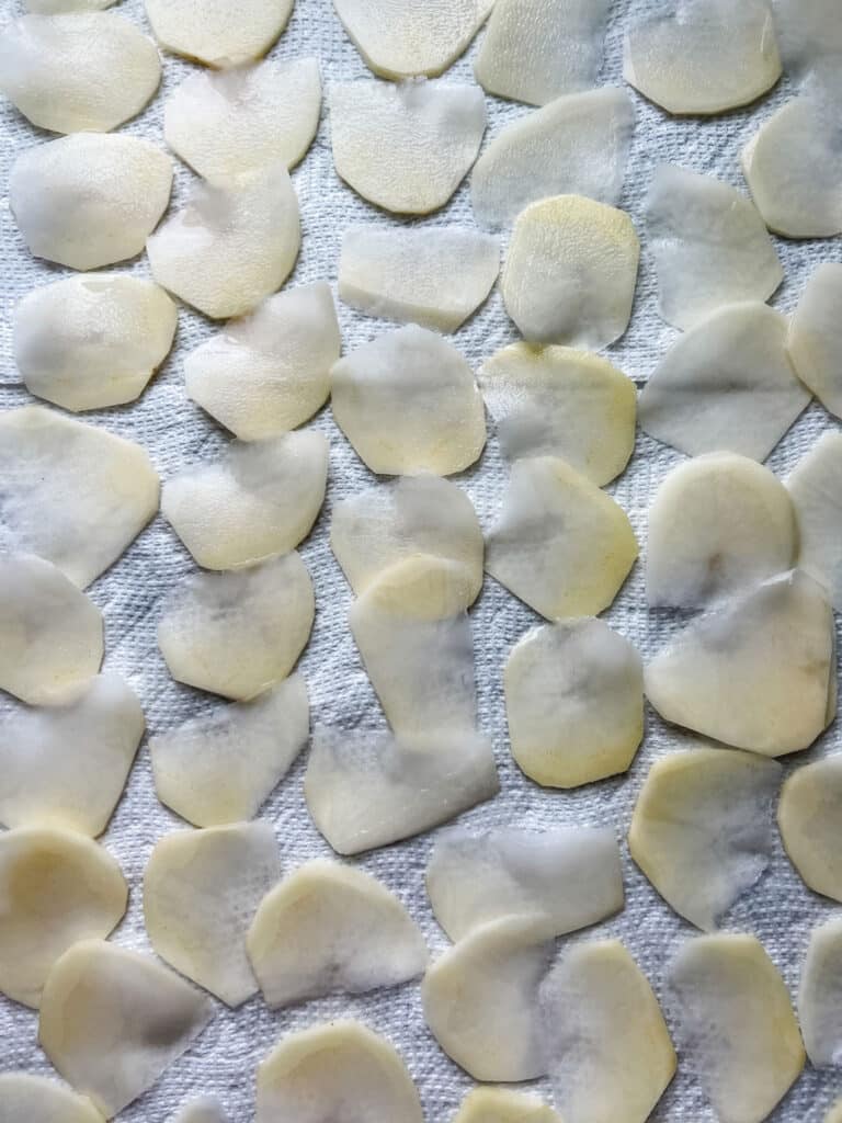 Sliced potatoes are drying on sheets of paper towels.
