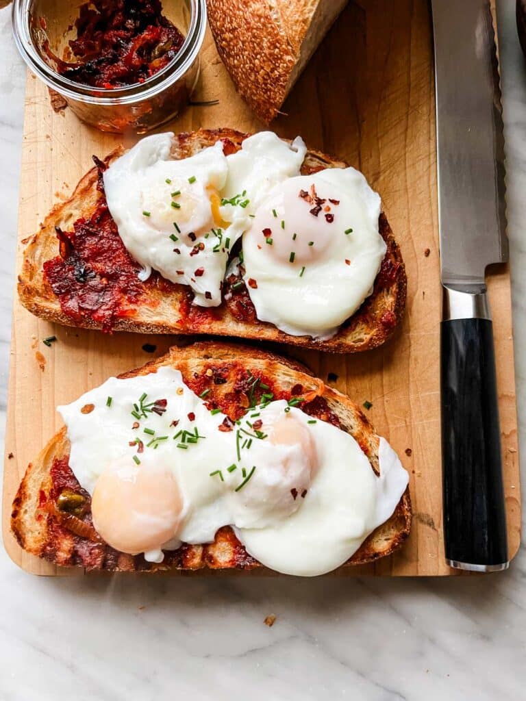 Toasted bread with shallot mixture spread is topped with two poached eggs with red pepper flakes and fresh chopped chives and is ready for serving.