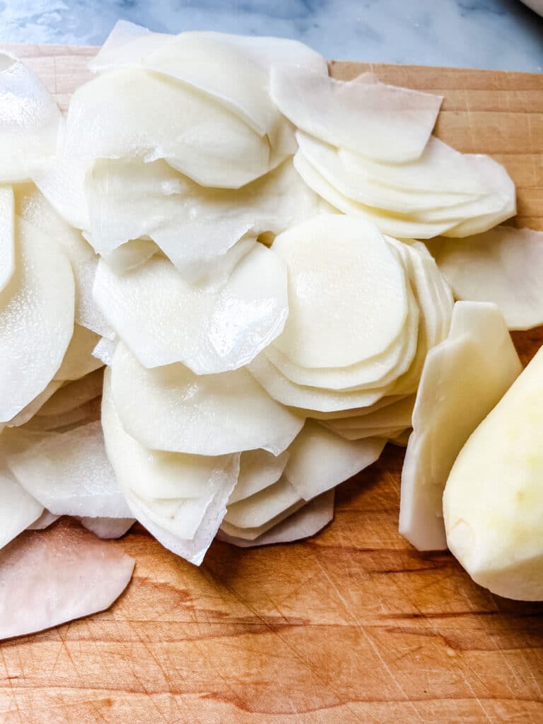 Sliced potatoes are sitting on a wooden cutting board.