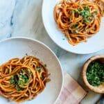 Caramelized shallot pasta is served in two white bowls. Next to the bowls is chopped parsley and garlic for garnishing.