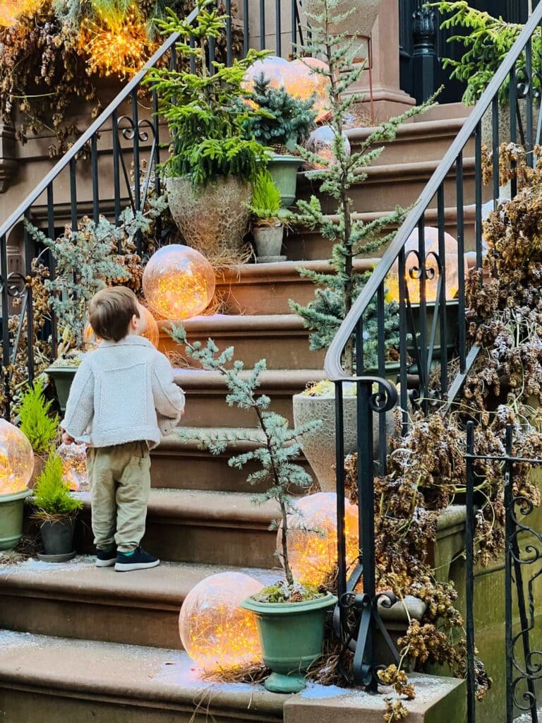 A little boy stands on the steps of a Brooklyn townhouse admiring the magic of Christmas decorations.