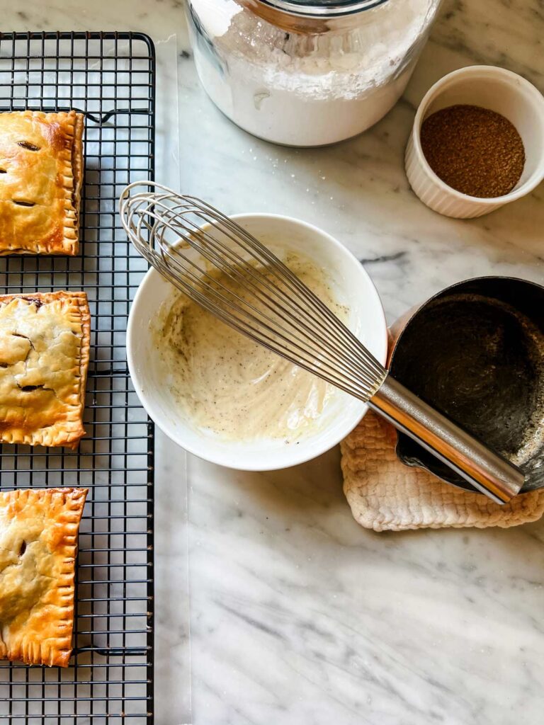 Homemade apple pie pop tarts rest on a wire cooling rack ready to be glazed with brown butter icing.