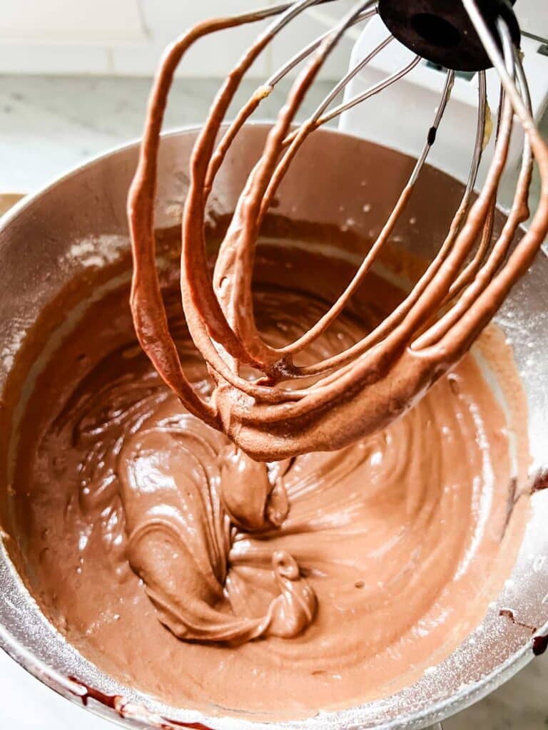 The hot chocolate bundt cake batter has been mixed in a stand mixer and is ready to pour into individual molds.