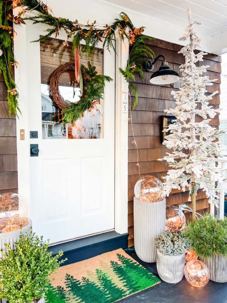 Christmas trees, garland and magical globe lights adorn this beautiful front porch welcoming all for the holidays.