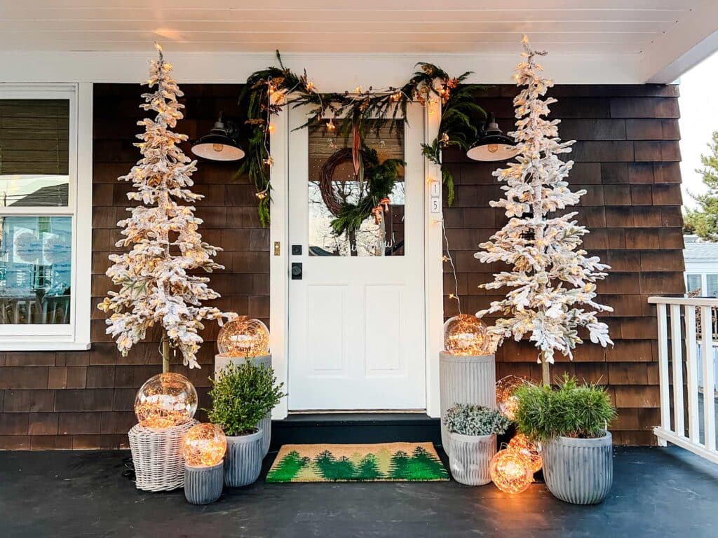Two Christmas trees on each side of a door with magical glow light balls in some pots and greenery in others make this Christmas and winter front porch 2023. 