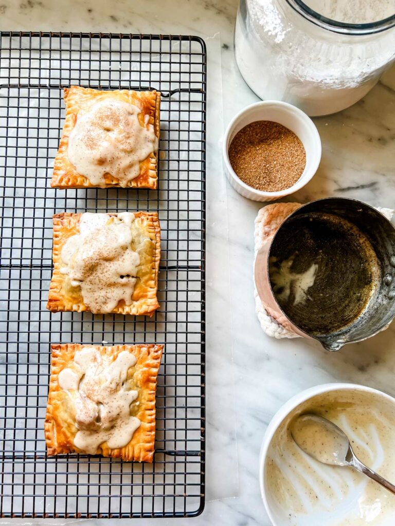 Homemade apple pie pop tarts on a cooling rack freshly glazed with brown butter icing and sprinkled with turbinato sugar.